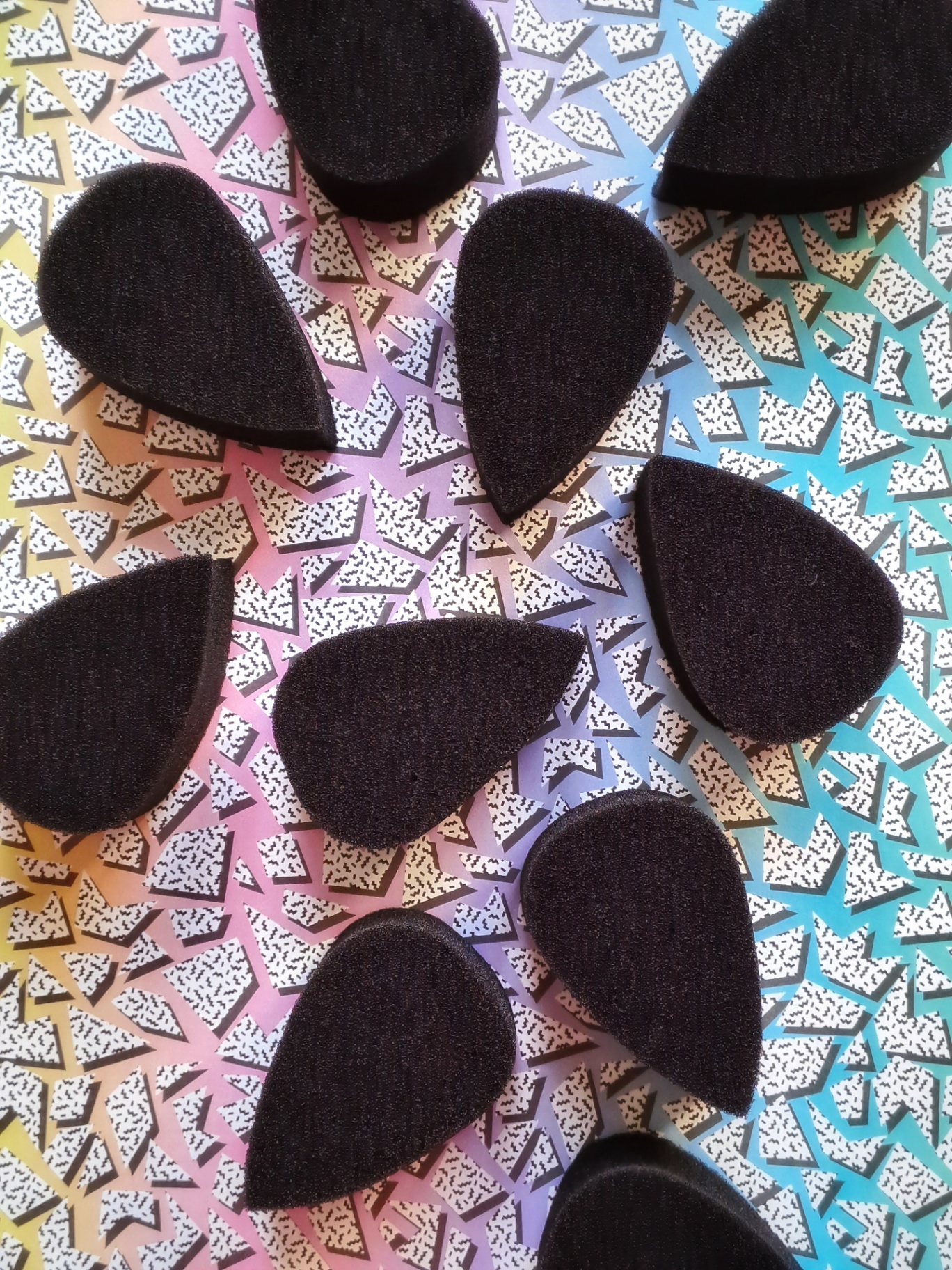 Black teardrop face paint sponges arranged on a pastel pattern